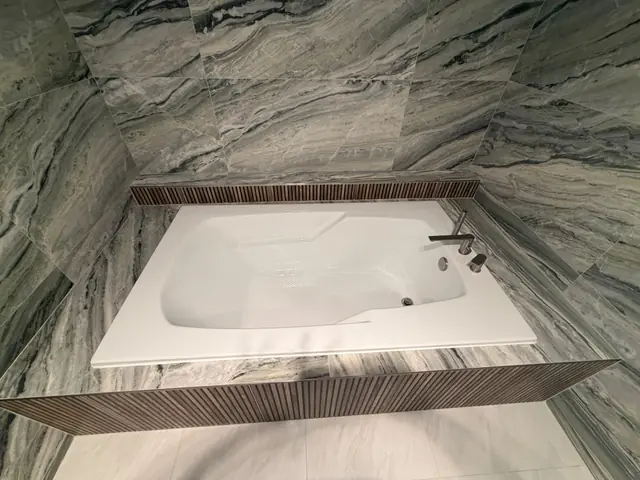 Drop-in soaking tub surrounded by large-format marble-look tile