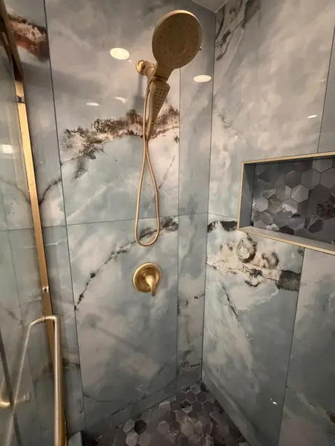Shower with gold fixtures and hexagon mosaic niche