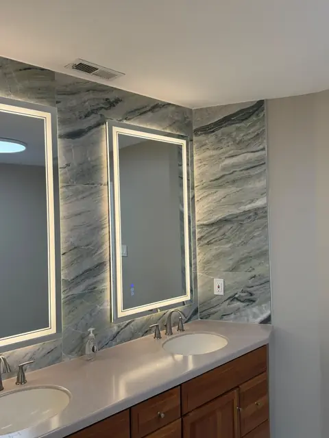 Double vanity with backlit mirrors and marble-look tile wall