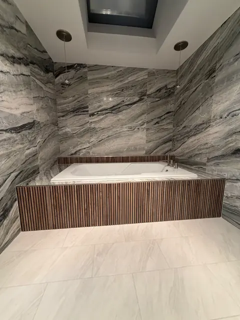 Soaking tub under a skylight with marble-look tile walls