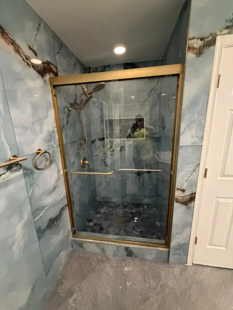 Glass shower with gold fixtures and blue marble-look tile